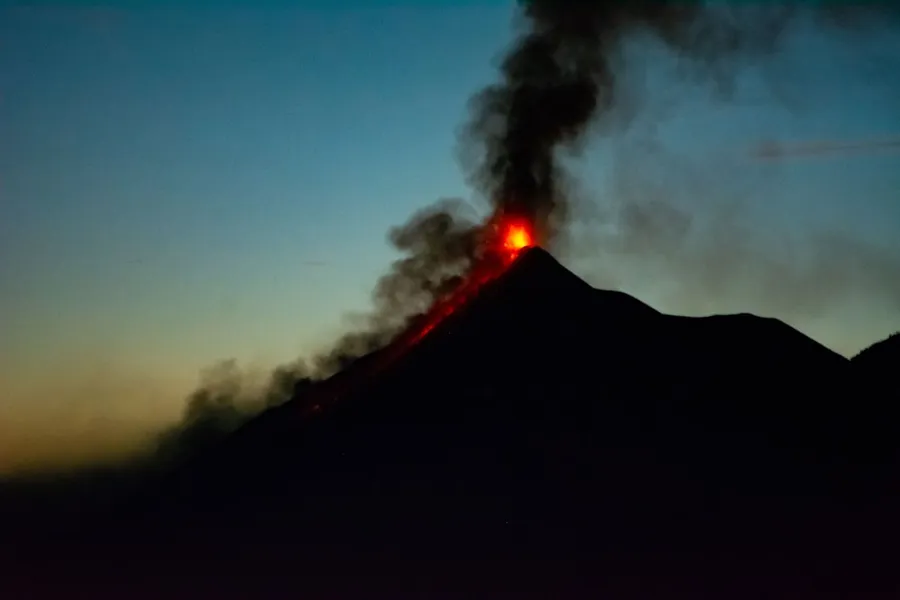 Volcano erupting against orange sunset sky