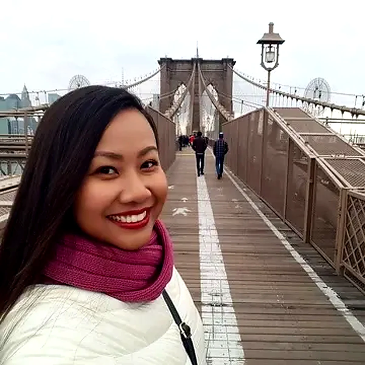 Woman with a pink scarf smiling on the Brooklyn Bridge walkway